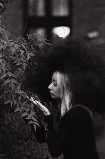 Black and white image of a woman contemplating, surrounded by nature, wearing a dramatic tulle hat