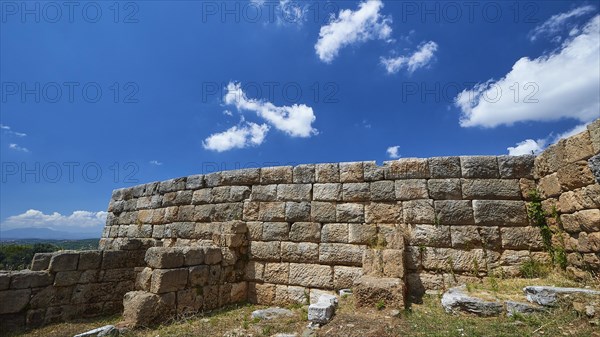 An ancient wall of stones under a blue sky with fluffy clouds, Ancient city wall, Archaeological site, Ancient Messene, Capital of Messinia, Messini, Peloponnese, Greece, Europe