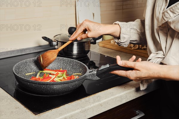 Unrecognizable woman stirring vegetable dressing with wooden spatula in frying pan