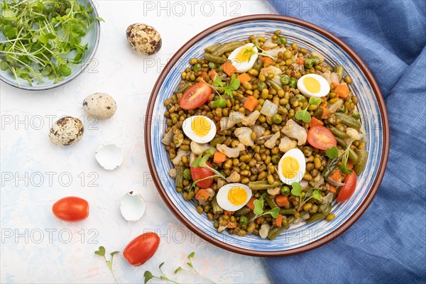 Mung bean porridge with quail eggs, tomatoes and microgreen sprouts on a white concrete background and blue textile. Top view, flat lay, close up