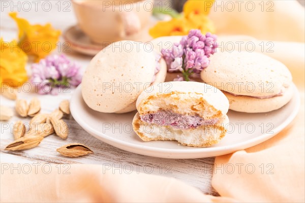 Meringues cakes with cup of coffee on a white wooden background and orange linen textile. Side view, close up, selective focus