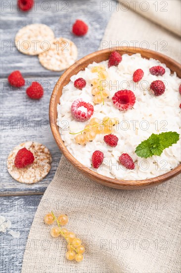 Rice flakes porridge with milk and strawberry in wooden bowl on gray wooden background and linen textile. Side view, selective focus, close up