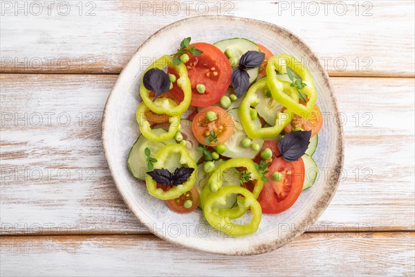 Vegetarian salad from green pea, tomatoes, pepper and basil on white wooden background. top view, close up, flat lay