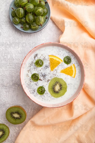 Yogurt with kiwi, gooseberry, chia in ceramic bowl on gray concrete background and orange linen textile. top view, flat lay, close up