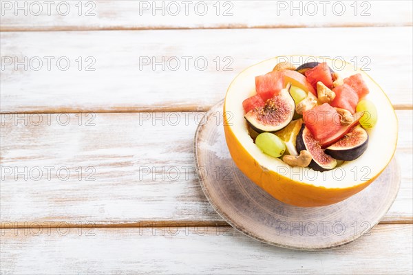 Vegetarian fruit salad of watermelon, grapes, figs, pear, orange, cashew on white wooden background. Side view, copy space, close up