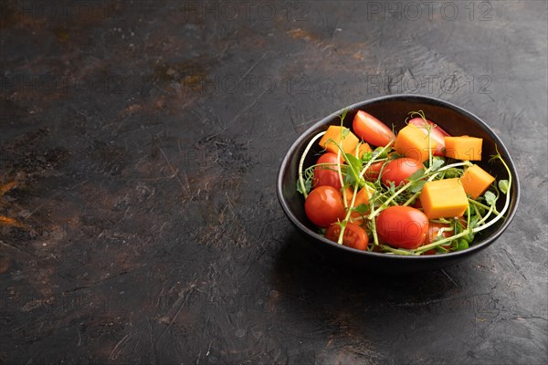 Vegetarian vegetable salad of tomatoes, pumpkin, microgreen pea sprouts on black concrete background. Side view, copy space, close up