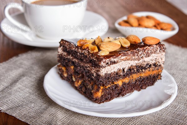 Chocolate cake with caramel, peanuts and almonds on a brown wooden background. cup of coffee, close up