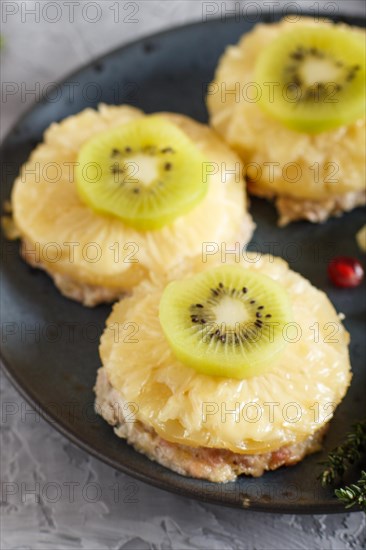 Pieces of baked pork with pineapple, cheese and kiwi on gray background, top view, close up, selective focus