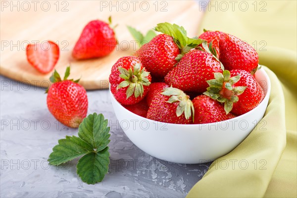 Fresh red strawberry in white bowl on gray concrete background. side view, close up, selective focus