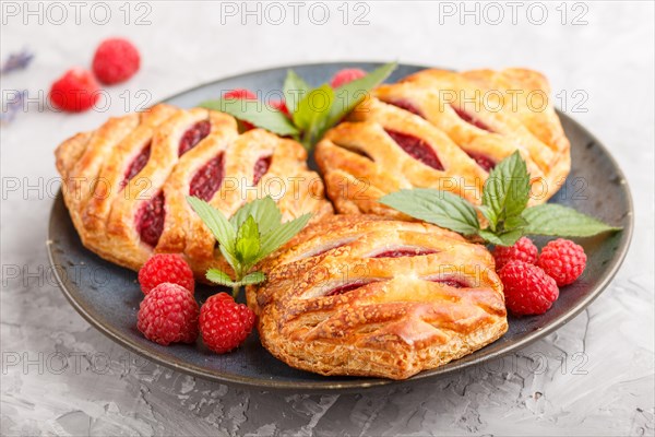 Puff pastry buns with strawberry jam on blue ceramic plate on gray concrete background, mint leaves. side view, close up, selective focus