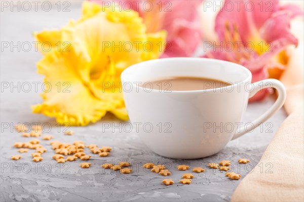 Yellow anf purple day-lilies cup of coffee on a gray concrete background, with orange textile. Morninig, spring, fashion composition, side view, close up, selective focus