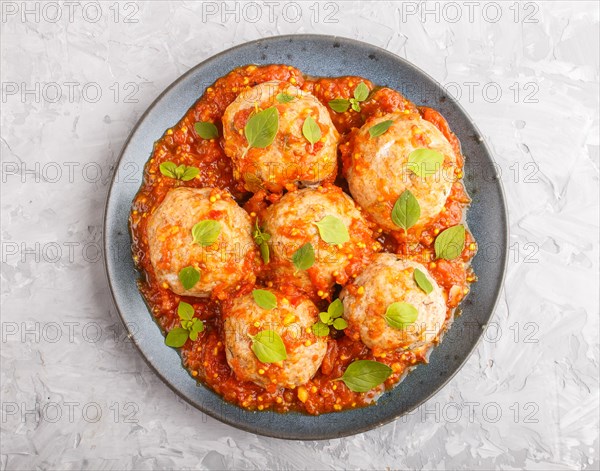 Pork meatballs with tomato sauce, oregano leaves, spices and herbs on blue ceramic plate on a gray concrete background. top view, flat lay, close up