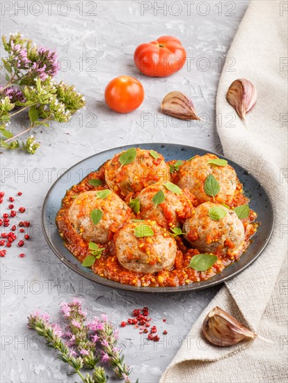 Pork meatballs with tomato sauce, oregano leaves, spices and herbs on blue ceramic plate on a gray concrete background with linen textile. side view, close up