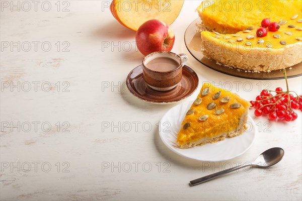 Traditional american sweet pumpkin pie decorated with hawthorn red berries and pumpkin seeds with cup of coffee on a white wooden background. side view, copy space