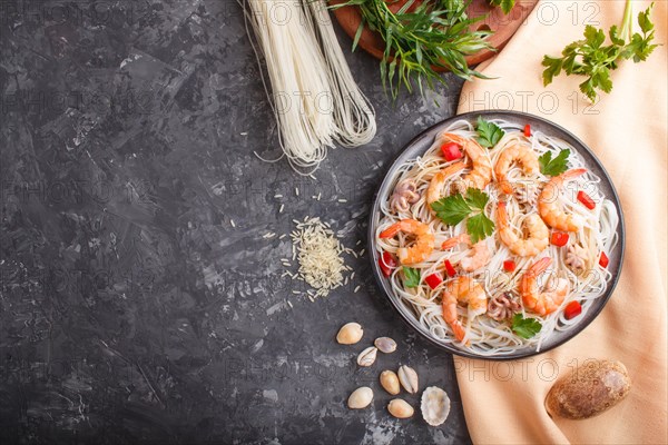 Rice noodles with shrimps or prawns and small octopuses on gray ceramic plate on a black concrete background and orange textile. Top view, flat lay, copy space