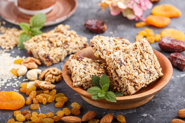 Homemade granola from oat flakes, dates, dried apricots, raisins, nuts with a cup of coffee on a black concrete background. Side view, close up, selective focus