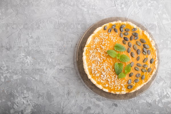 Traditional american sweet pumpkin pie decorated with mint, sesame and pumpkin seeds on a gray concrete background. top view, flat lay, copy space