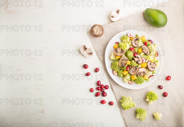 Vegetarian salad from romanesco cabbage, champignons, cranberry, avocado and pumpkin on a white wooden background and linen textile. top view, copy space, flat lay