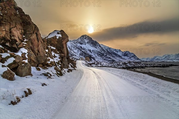 Eine vereiste gebogene Strasse auf den winterlichen Vesteralen mit verschneiten Bergen und einem Fjord
