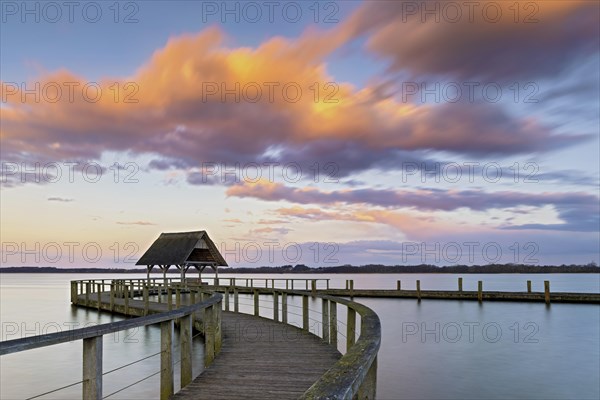 The well-known curved wooden footbridge in the evening light with pink clouds on Lake Hellendorf as a long exposure