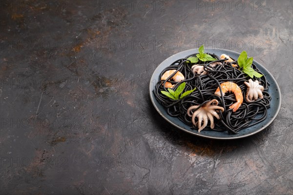 Black cuttlefish ink pasta with shrimps or prawns and small octopuses on black concrete background. Side view, copy space