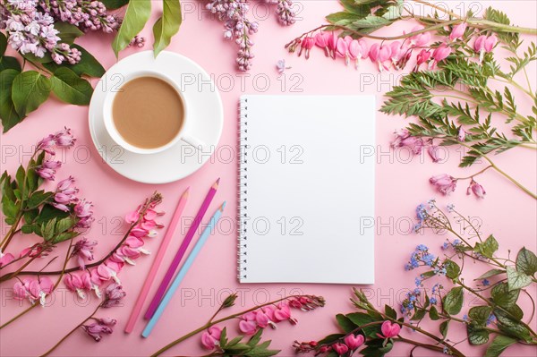 Purple lilac and bleeding heart flowers and a cup of coffee with notebook and colored pencils on pastel pink background. Morninig, spring, fashion composition. Flat lay, top view