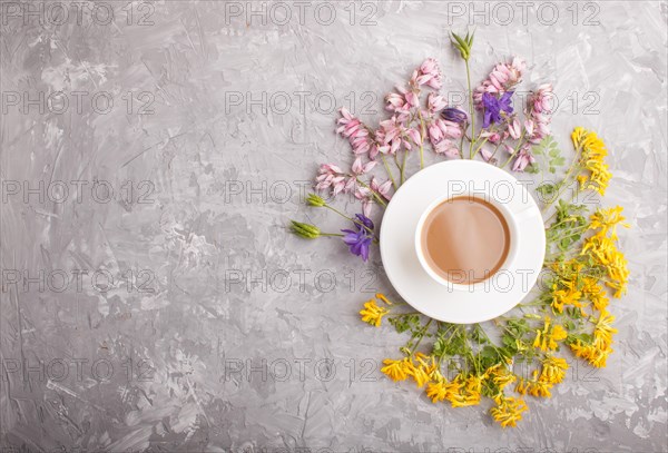 Yellow, pink and blue flowers in a spiral and a cup of coffee on a gray concrete background. Morninig, spring, fashion composition. Flat lay, top view, copy space