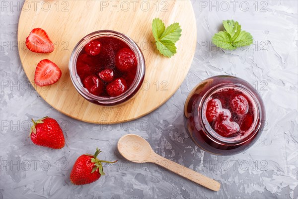 Strawberry jam in a glass jar with berries and leaves on gray concrete background. Homemade, top view, flat lay