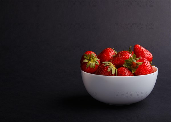 Fresh red sweet cherry in white bowl on black background. side view, copy space