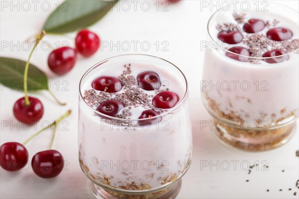 Yoghurt with cherries, chia seeds and granola in glass with wooden spoon on white wooden background. side view, close up, selective focus