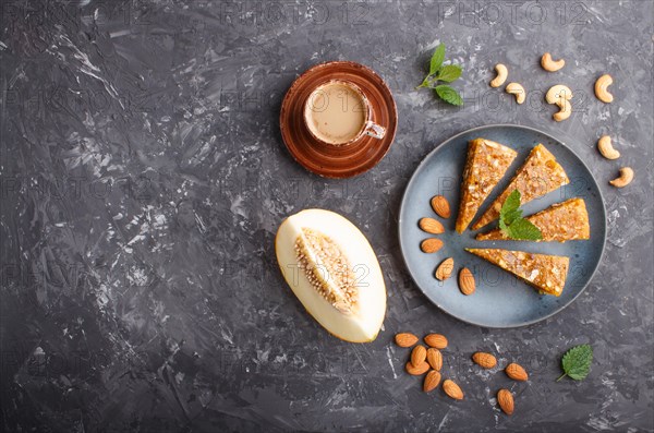 Traditional turkish candy cezerye made from caramelised melon, roasted walnuts, hazelnuts, cashew, pistachios in blue ceramic plate and a cup of coffee on a black concrete background. top view, flat lay, copy space