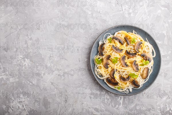 Rice noodles with champignons mushrooms, egg sauce and oregano on blue ceramic plate on a gray concrete background. Top view, flat lay, copy space