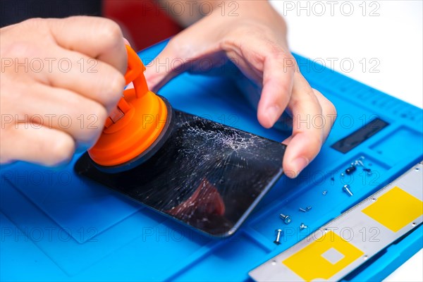 Close-up of the hands of a repairman using a suction cup to lift a broken screen of a mobile phone in the repair shop