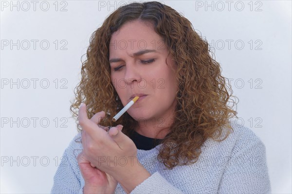 Attractive blonde curly-haired woman lighting a cigarette with white background and copy space