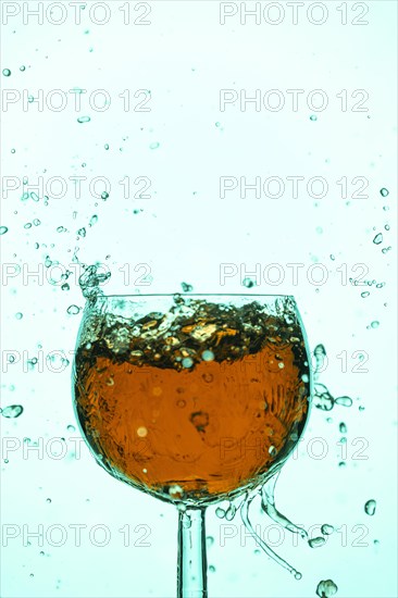 Splashing liquid in orange and turquoise in a wine glass, blue background