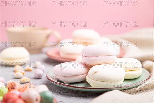 Colored zephyr or marshmallow with cup of coffee and dragees on a gray and pink background and linen textile. Side view, close up, selective focus