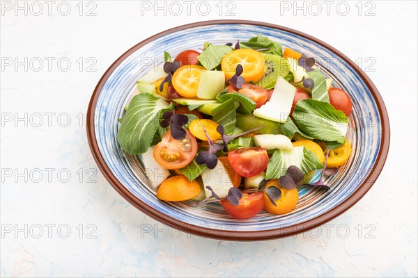 Vegetarian salad of pac choi cabbage, kiwi, tomatoes, kumquat, microgreen sprouts on a white concrete background. Side view, close up