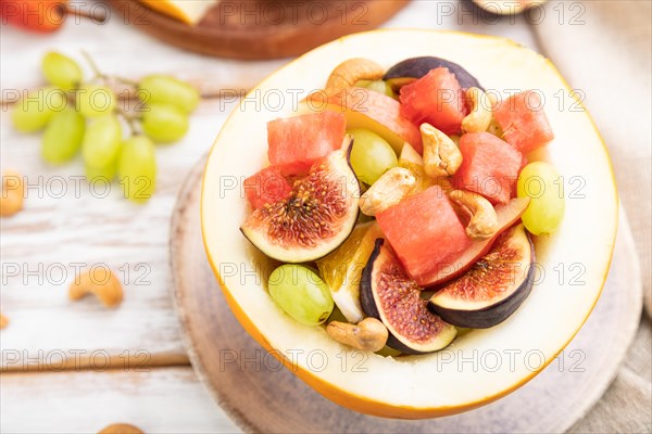 Vegetarian fruit salad of watermelon, grapes, figs, pear, orange, cashew on white wooden background and linen textile. Side view, close up, selective focus