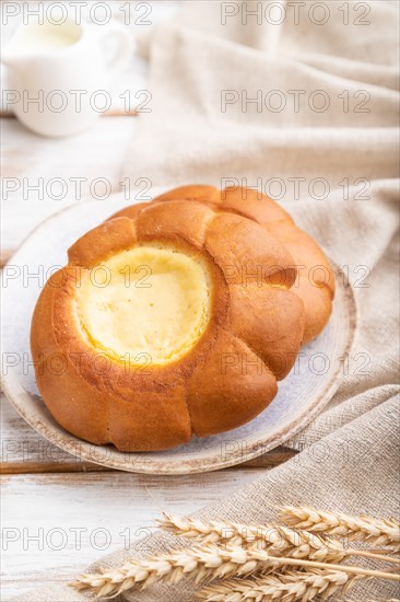 Sour cream bun with cup of coffee on a white wooden background and linen textile. Side view, close up, selective focus