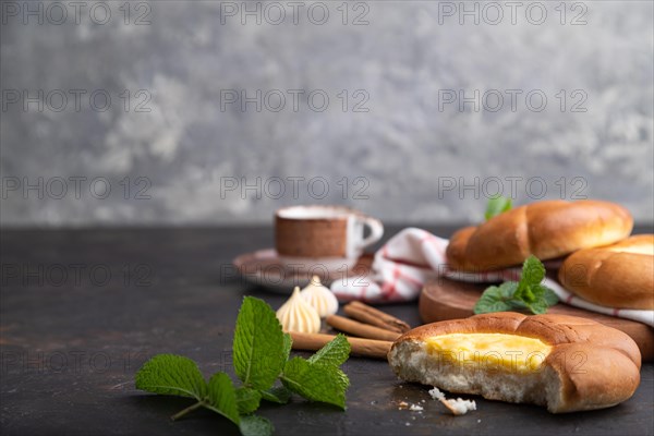 Sour cream bun with cup of coffee on a black concrete background and linen textile. Side view, copy space