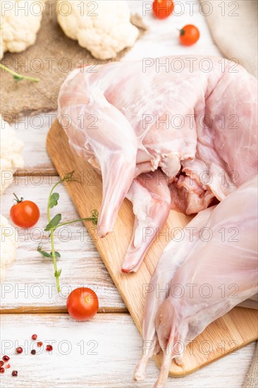 Whole raw rabbit with cauliflower, tomatoes and spices on a white wooden background and linen textile. Side view, close up, selective focus