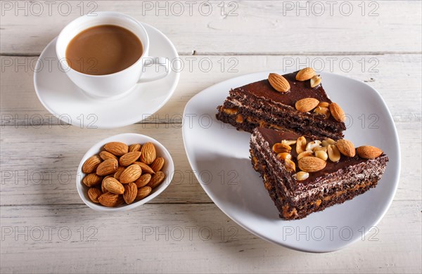 Chocolate cake with caramel, peanuts and almonds on a white wooden background. cup of coffee, top view, close up
