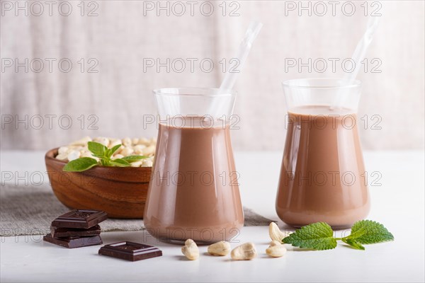 Organic non dairy cashew chocolate milk in glass and wooden plate with cashew nuts on a gray concrete background. Vegan healthy food concept, close up, side view