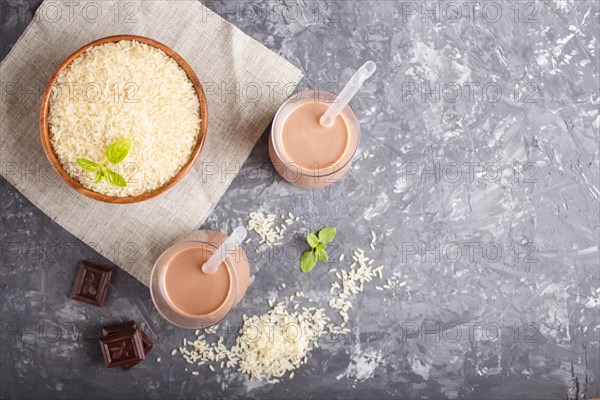 Organic non dairy rice chocolate milk in glass and wooden plate with rice seeds on a black concrete background. Vegan healthy food concept, flat lay, top view, copy space