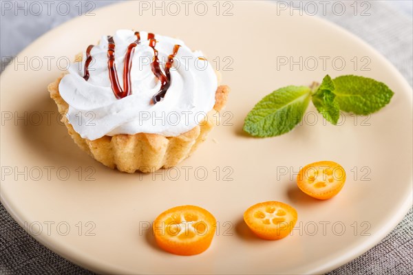 Cake with whipped egg cream on a light brown plate with kumquat slices and mint leaves on a gray concrete background with linen napkin. selective focus, close up. side view