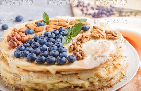 Homemade layered Napoleon cake with milk cream. Decorated with blueberry, almonds, walnuts, hazelnuts, mint on a gray concrete background. side view, selective focus, close up