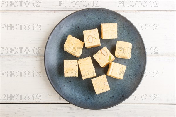 Traditional indian candy soan papdi in a blue ceramic plate with almond and pistache on a white wooden background. top view, flat lay, close up
