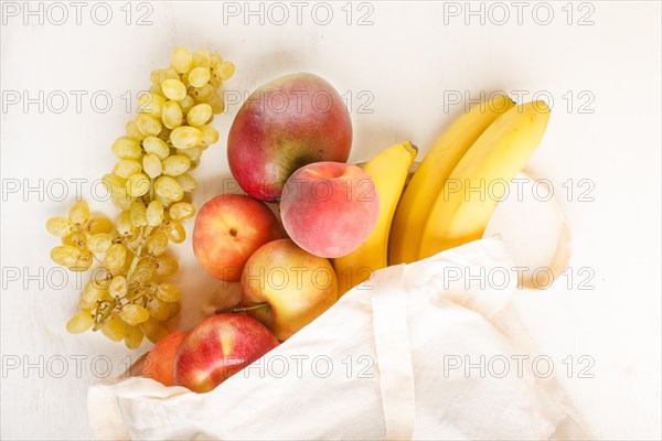 Fruits in reusable cotton textile white bag. Zero waste shopping, storage and recycling concept, eco friendly lifestyle. Top view, flat lay, close up. Peach, apple, mango, grape, banana