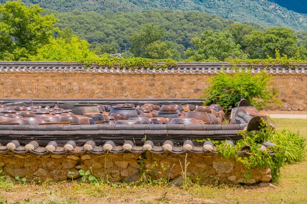 Rows of brown ceramic pickling jars sitting in walled enclosure of stone and mortar with tiled shingles in South Korea