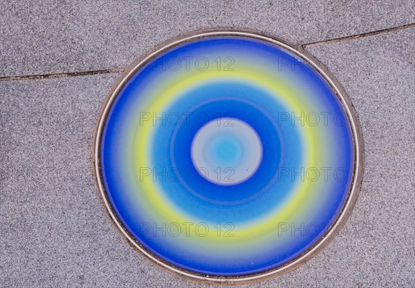 Closeup round glass of blue, yellow and white inlaid in concrete sidewalk in public park in South Korea